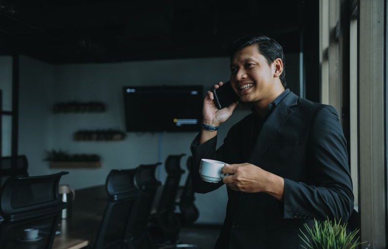 Success Measurement - smiling man holding cup and using smartphone