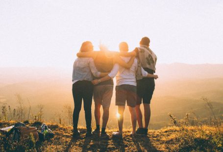 Culture Community - four person hands wrap around shoulders while looking at sunset