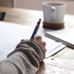 Personal Story - person writing on brown wooden table near white ceramic mug