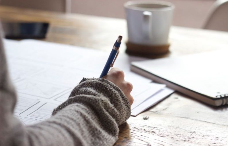 Personal Story - person writing on brown wooden table near white ceramic mug